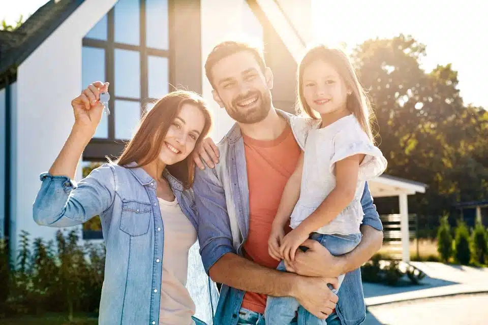 Man, woman, and child standing in front of their new custom built home holding the keys and smiling.