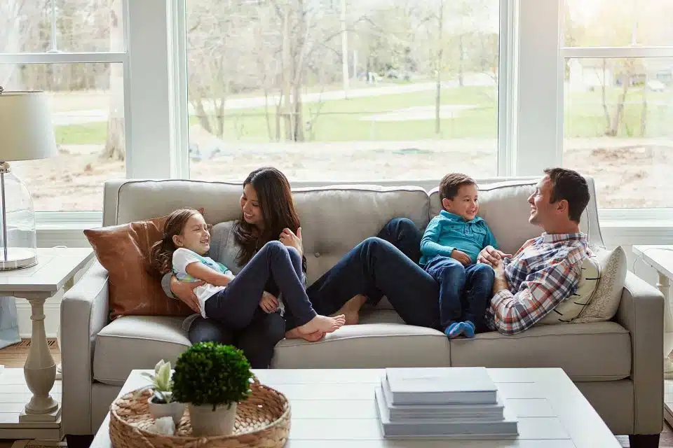 Family of four sitting on a couch in front of a large window.